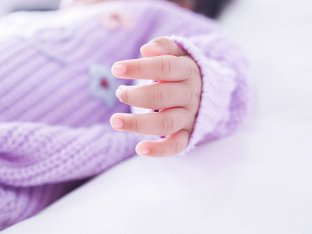 Close up of newborn baby hand is wearing a purple clothes on white bedの写真素材