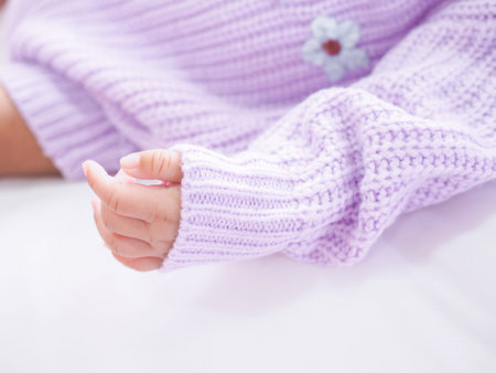 Close up of newborn baby hand is wearing a purple clothes on white bedの写真素材