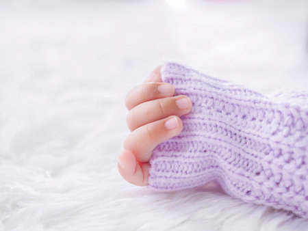 Close up of newborn baby hand is wearing a purple clothes on white bedの写真素材