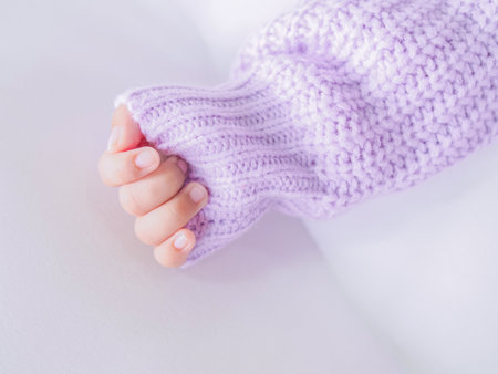 Close up of newborn baby hand is wearing a purple clothes on white bedの写真素材