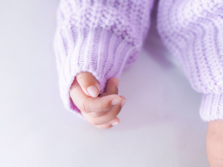 Close up of newborn baby hand is wearing a purple clothes on white bedの写真素材