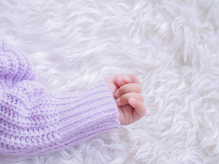 Close up of newborn baby hand is wearing a purple clothes on white bedの写真素材