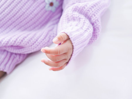 Close up of newborn baby hand is wearing a purple clothes on white bedの写真素材