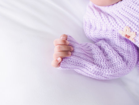 Close up of newborn baby hand is wearing a purple clothes on white bedの写真素材