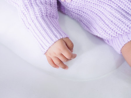 Close up of newborn baby hand is wearing a purple clothes on white bedの写真素材