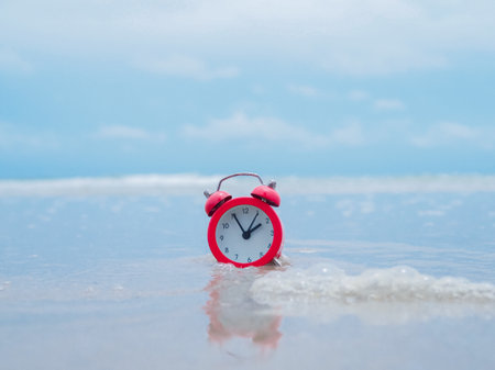 Red alarm clock on the beach with ocean waves. The concept about Time to summer, Travel, Vacation and Relaxationの写真素材