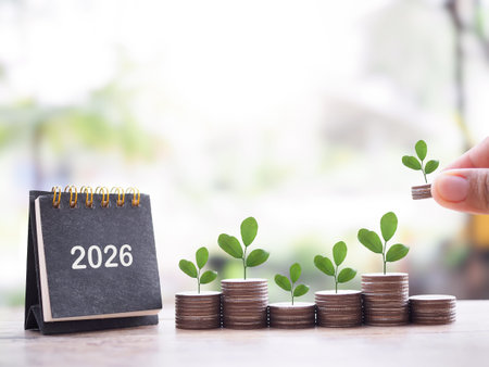 Close up hand putting coin into stack of coins and 2026 desk calendar. The concept of saving money,...