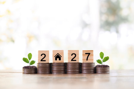 Wooden blocks with the number 2027 and plants growing up on stack of coins. The concept of saving...