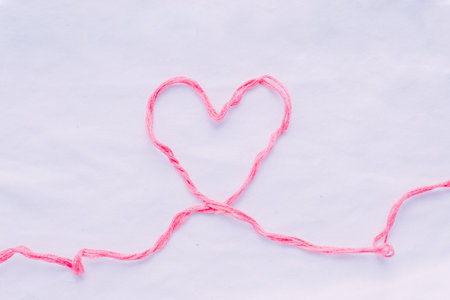 Pink thread in the shape of a heart on a white background.の写真素材