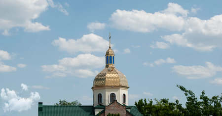 Dome of a church with a cross in sunny weather with clouds and trees