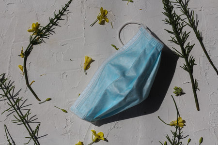 Blue protective face mask on a white background with green leaves and white flowers. Horizontal...