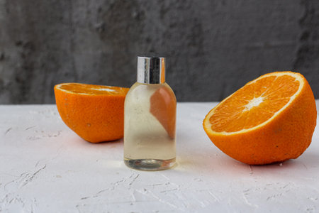 A clear transparent beauty product bottle standing on a white background surrounded by fresh oranges. Horizontal imageの写真素材