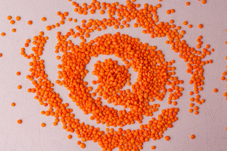 Composition flat lay of Raw lentils in form of galaxy. Orange grains on pale pink background. Concept of healthy eco vegan foodの写真素材
