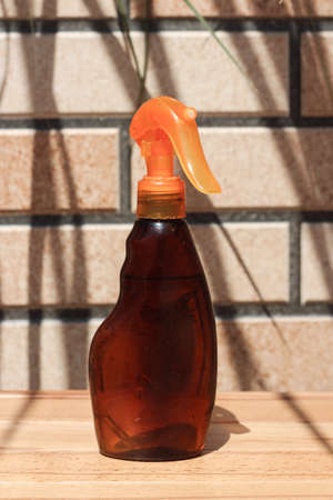 Brown bottle for mock up for sunblock spray or tanning oil spray. A bottle standing on a yellow surface in front of brick wall background. palm leaves shadows add summer mood to the pitureの写真素材