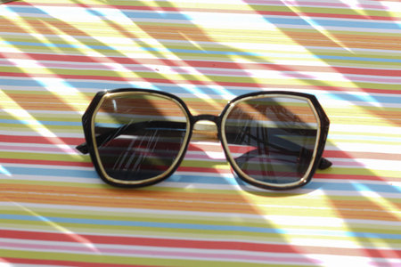 Modern black sunglasses on a bright colorful striped background under the sun. Background with contrasted shadows. Reflection of palm leaves in the lens of sunglassesの写真素材
