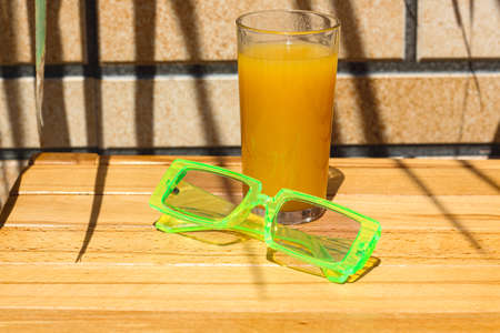 Summertime wallpaper in bright vivid colors. A composition of a glass of orange juice and modern trendy light green sunglassesの写真素材