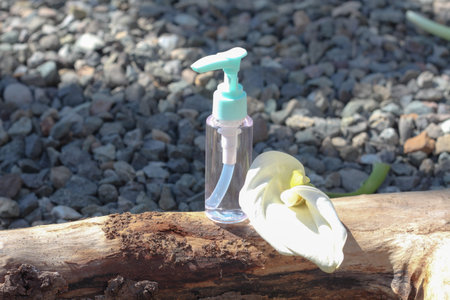 A clear sanitizer bottle standing on tree thick branch. Fresh white flower is added for decoration,...