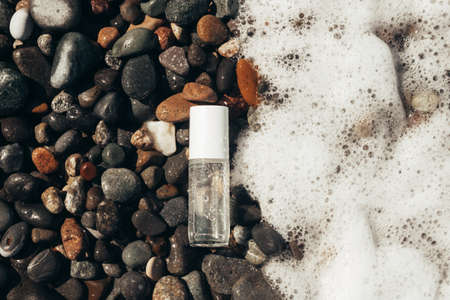 Beauty product transparent bottle on wet beach stones and surrounded by sea foam from the right. Fresh ocean scented product mock up.の写真素材