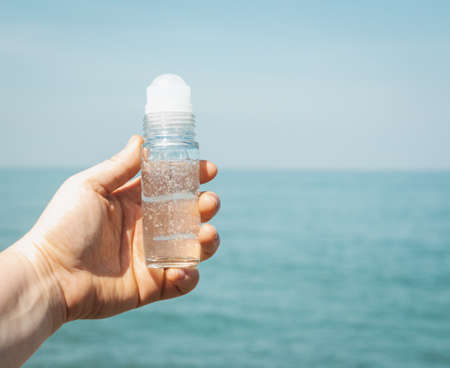Close up of a Girls hand holding deodorant transparent bottle outside in front of sea coast. Idea for fresh marine scented cosmetics mock up.の写真素材