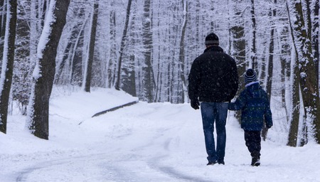 A man with his son is walking in a snow-covered forest.の写真素材