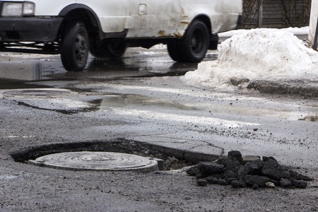 The car drives past the pothole with puddles on the roadの写真素材