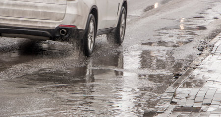 The car drives past the pothole with puddles on the road
