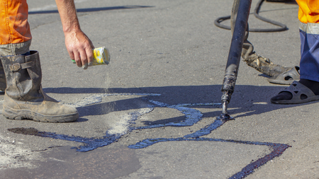 Workers repair the road, pour small cracks with bitumen to prevent further destruction of the road surface. Close upの写真素材