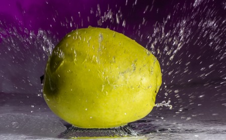 Green apple and splashes of water on a colored background close upの写真素材