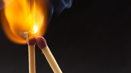 Burning wooden match with a red match head on a black background. Close up