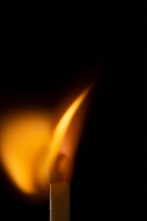 Burning wooden match with a red match head on a black background. Close up
