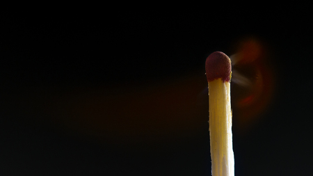 Burning wooden match with a red match head on a black background. Close upの写真素材