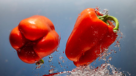 fresh water splash on red sweet pepper on blue background close up