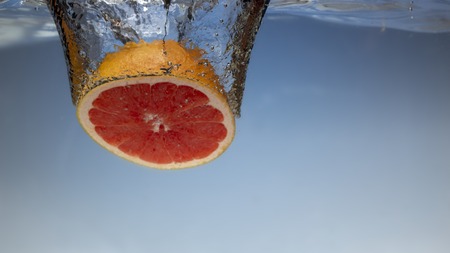 Fresh grapefruit with water splash on blue backgroundの写真素材