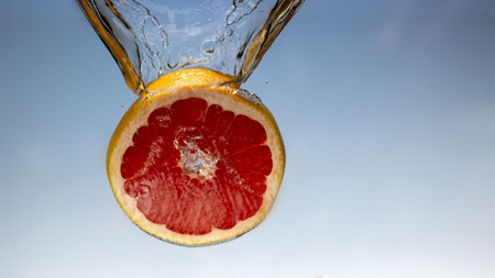 Fresh grapefruit with water splash on blue backgroundの写真素材