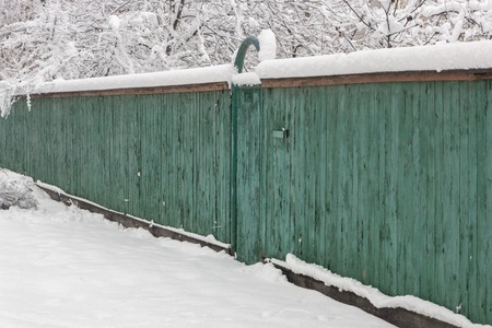 snow-covered boardwalk old green fence. Countryside, gloomy winter dayの写真素材