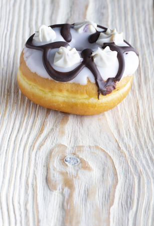 Fresh donut poured with icing and decorations, on a white textured wooden tableの写真素材