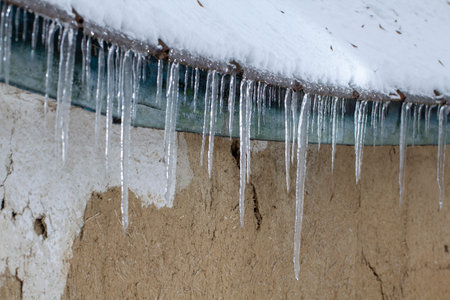 Icicles on an old, rusty, rural roof. Clay wall Close up