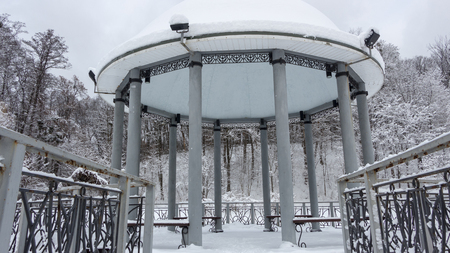 Snow-covered gazebo with a metal bridge in the middle of a lake in the park Winter backgroundの写真素材