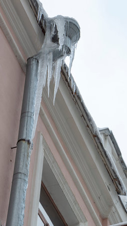 Icicles on the drainpipe and ditch. Incorrect installation of the drainage system, on which large icicles appear that pose a threat to the health and lives of peopleの写真素材