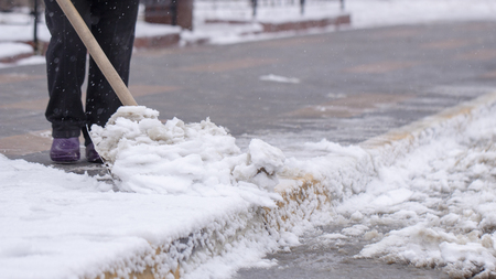 Man with snow shovel cleans sidewalks in winter street.の写真素材