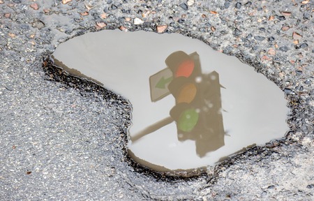 A working traffic light with a green arrow to the left reflected in a hollow of high water Close upの写真素材