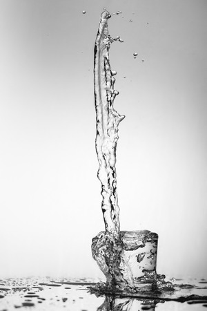 Pure drinking water with splashes in a round glass on a light green background close upの写真素材