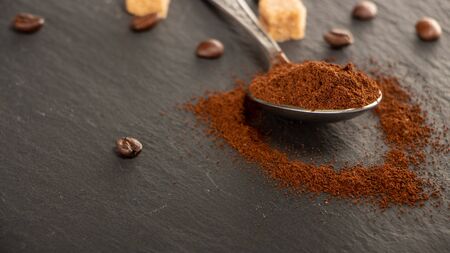 A metal spoon with ground coffee lies on a slate tray, on which coffee seeds are spread out. Backgroundの写真素材