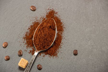 A metal spoon with ground coffee lies on a slate tray, on which coffee seeds are spread out. Backgroundの写真素材