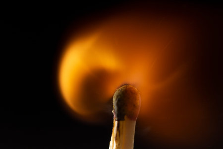 Burning wooden match with a red match head on a black background. Close up