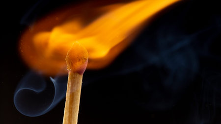 Burning wooden match with a red match head on a black background. Close up
