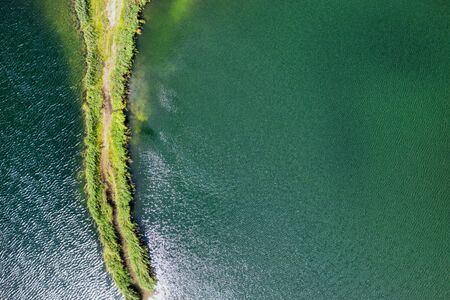 A small spit with a path covered with green grass on both sides, on a clear lake.の写真素材