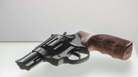 Black vintage revolver with wooden handle lying on glass table on light background, top view.の写真素材