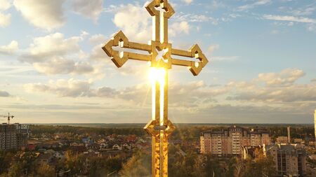 Gilded cross on the dome of the church. The sun's rays shine on the surface. The sky and the city in the background.の写真素材