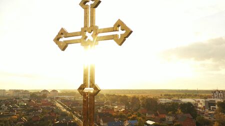Gilded cross on the dome of the church. The sun's rays shine on the surface. The sky and the city in the background.の写真素材